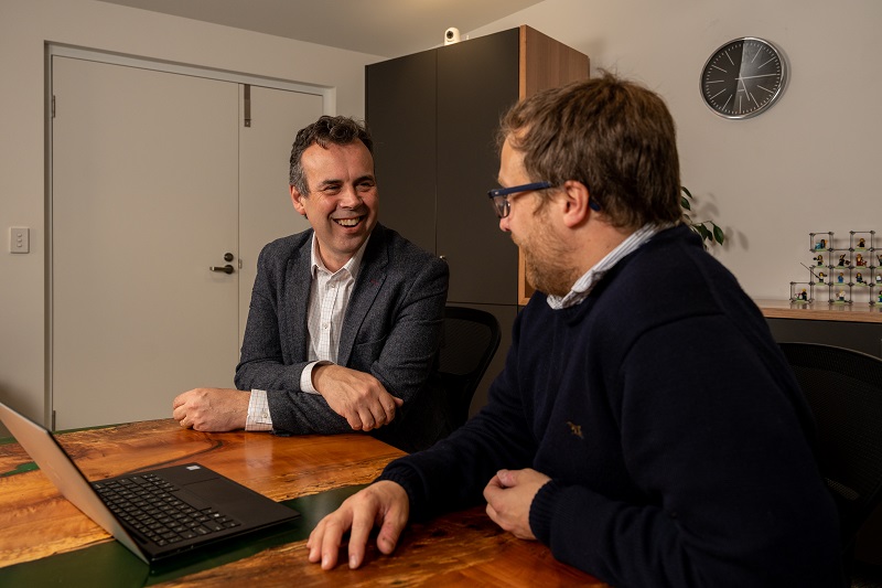 2 men sitting at a table looking at a laptop