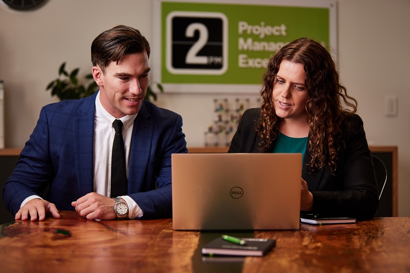 two people sitting at a desk looking at a laptop